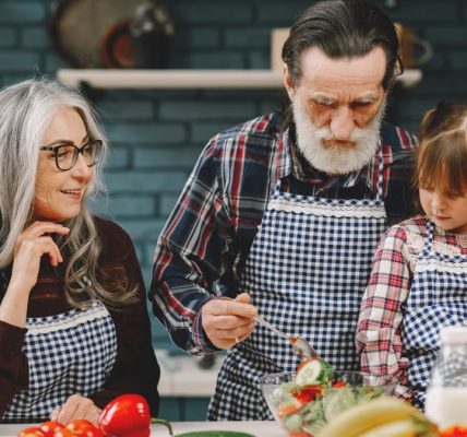 Grandparents and granddaughter preparing salad in home kitchen, creating memories together.