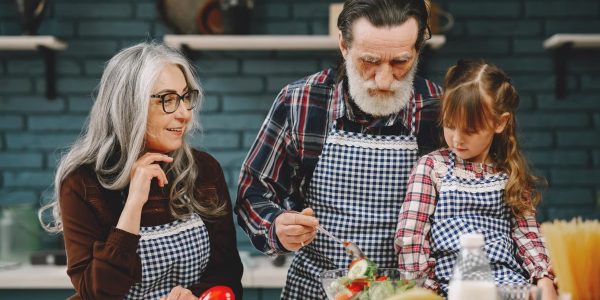 Grandparents and granddaughter preparing salad in home kitchen, creating memories together.